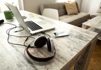 Pöytä, jossa auki oleva kannettava tietokone, puhelin ja kuulokkeet.