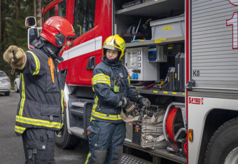 Kaksi palokuntalaista varusteissaan paloauton edessä.