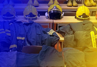 Pöydillä olevia paloasuja ja kypäriä, kuvassa sininen ja keltainen väritys.