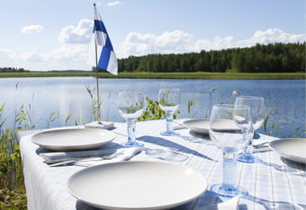 Pöytä on katettu järven rantaan, pöydällä pieni Suomen lippu.