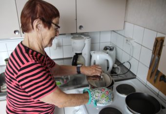 Iäkäs nainen valmistaa liedellä ruokaa.