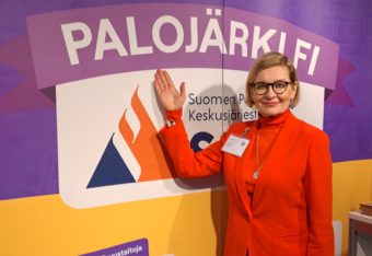 Paula Risikko osoittaa kädellään messuosaston seinällä olevaa Palojärki.fi-nimeä.