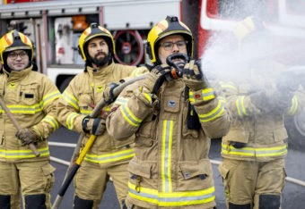 Palokuntalaisia suihkuavan sammutusletkun kanssa paloauton edessä.