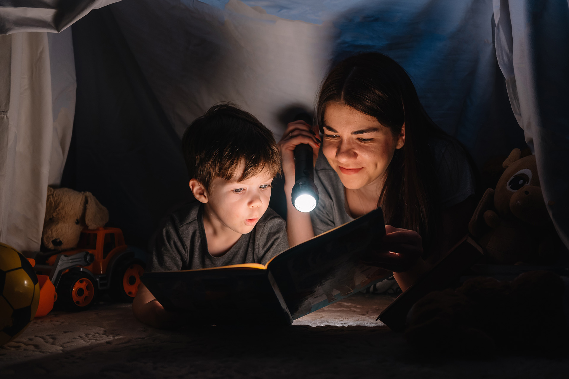Nainen ja lapsi lukevat kirjaa taskulampun valossa.