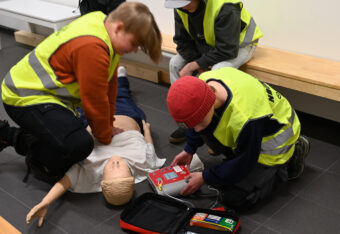 Nuoret harjoittelevat paineluelvytystä ja sydäniskurin käyttöä elvytysnukelle.