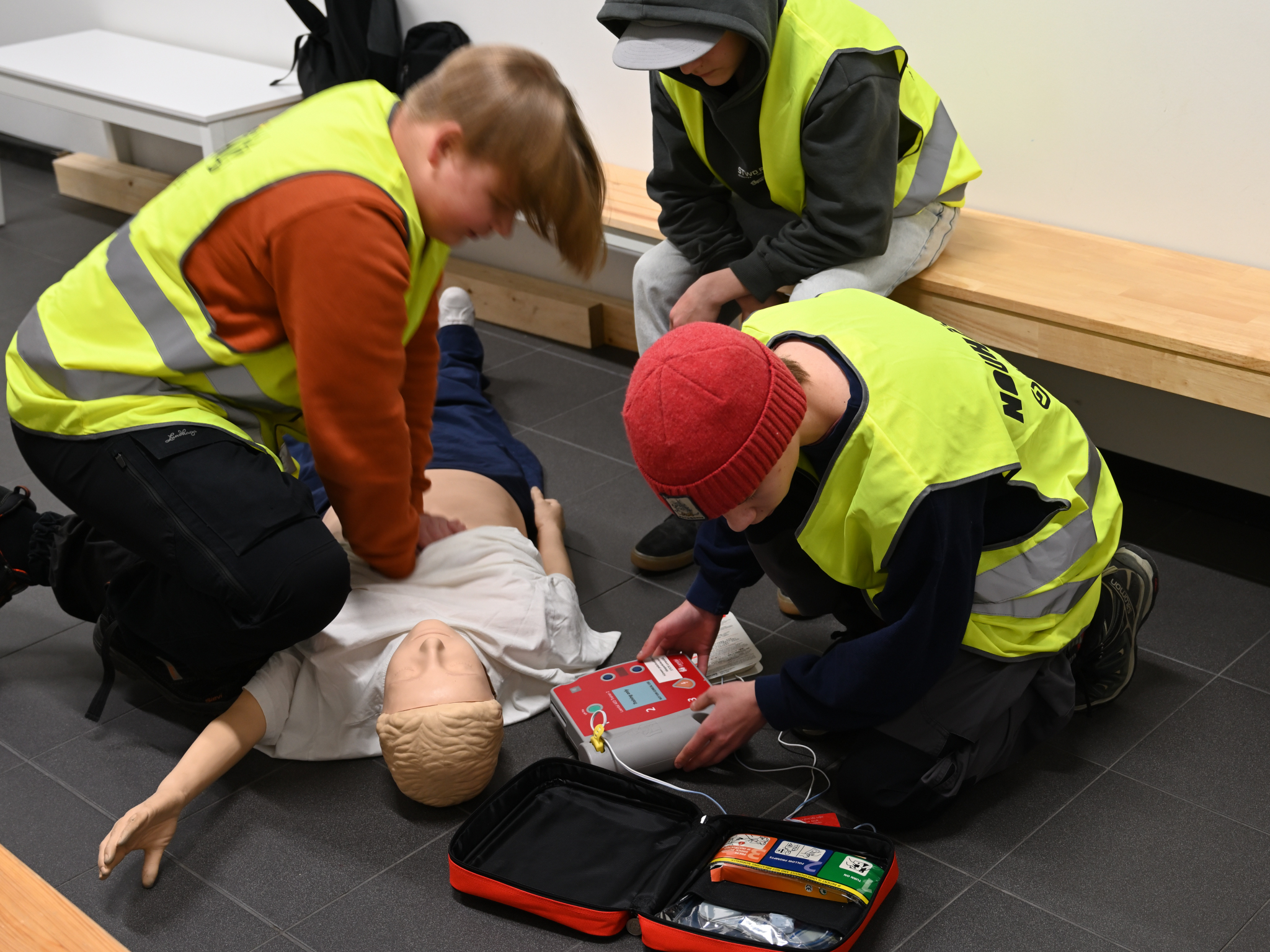 Nuoret harjoittelevat paineluelvytystä ja sydäniskurin käyttöä elvytysnukelle.
