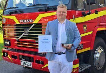 Vuoden palokuntanuori Samu Soikkeli poseeraa paloauton edessä ja pitelee käsissään kunniakirjaa ja palkintoa.