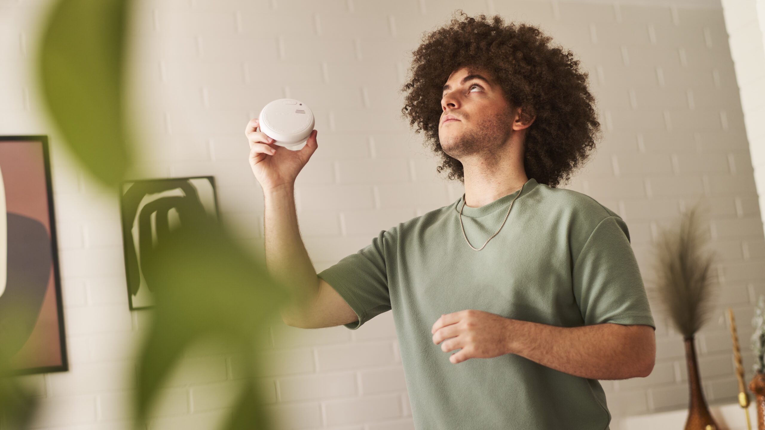 Nuori mies pitää palovaroitinta kädessä ja katsoo mietteliäänä ylös kattoon.