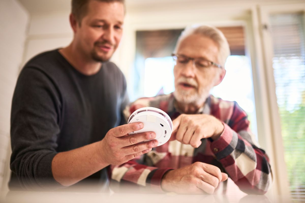 Aikuinen mies ja iäkkäämpi mies tutkivat palovaroitinta.