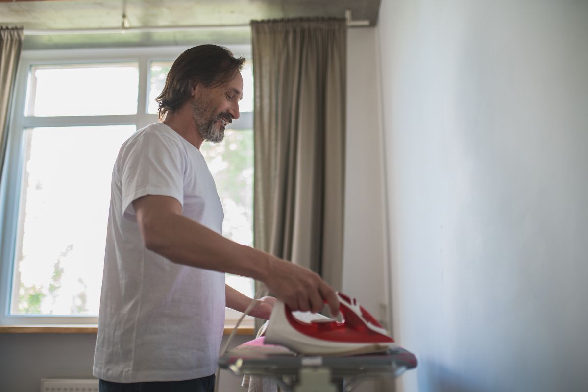 A middle-aged man is happily using an iron.