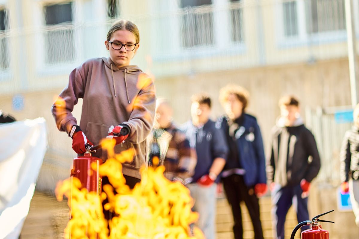 Student puts out a fire with a hand extinguisher during a NouHätä-lesson.