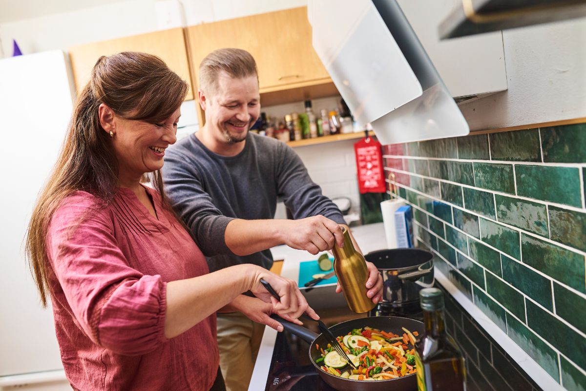Pariskunta kokkailee, sammutuspeite näkyy keittiön seinällä.