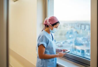 Sairaanhoitaja työasussa ikkunan edessä.