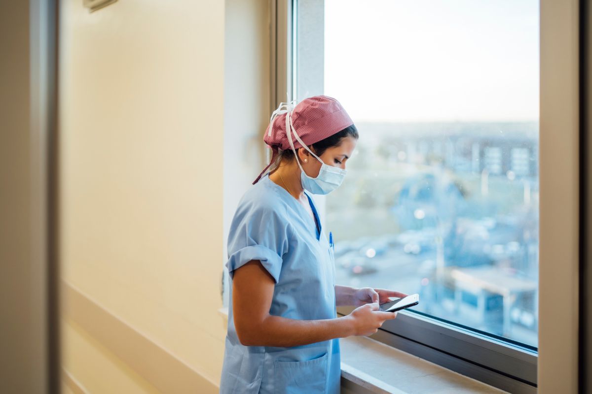 Sairaanhoitaja työasussa ikkunan edessä.
