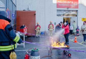Kävijä harjoittelee palon sammuttamista käsisammuttimella Päivä Paloasemalla -tapahtumassa. Palokuntalaiset auttavat harjoittelussa.