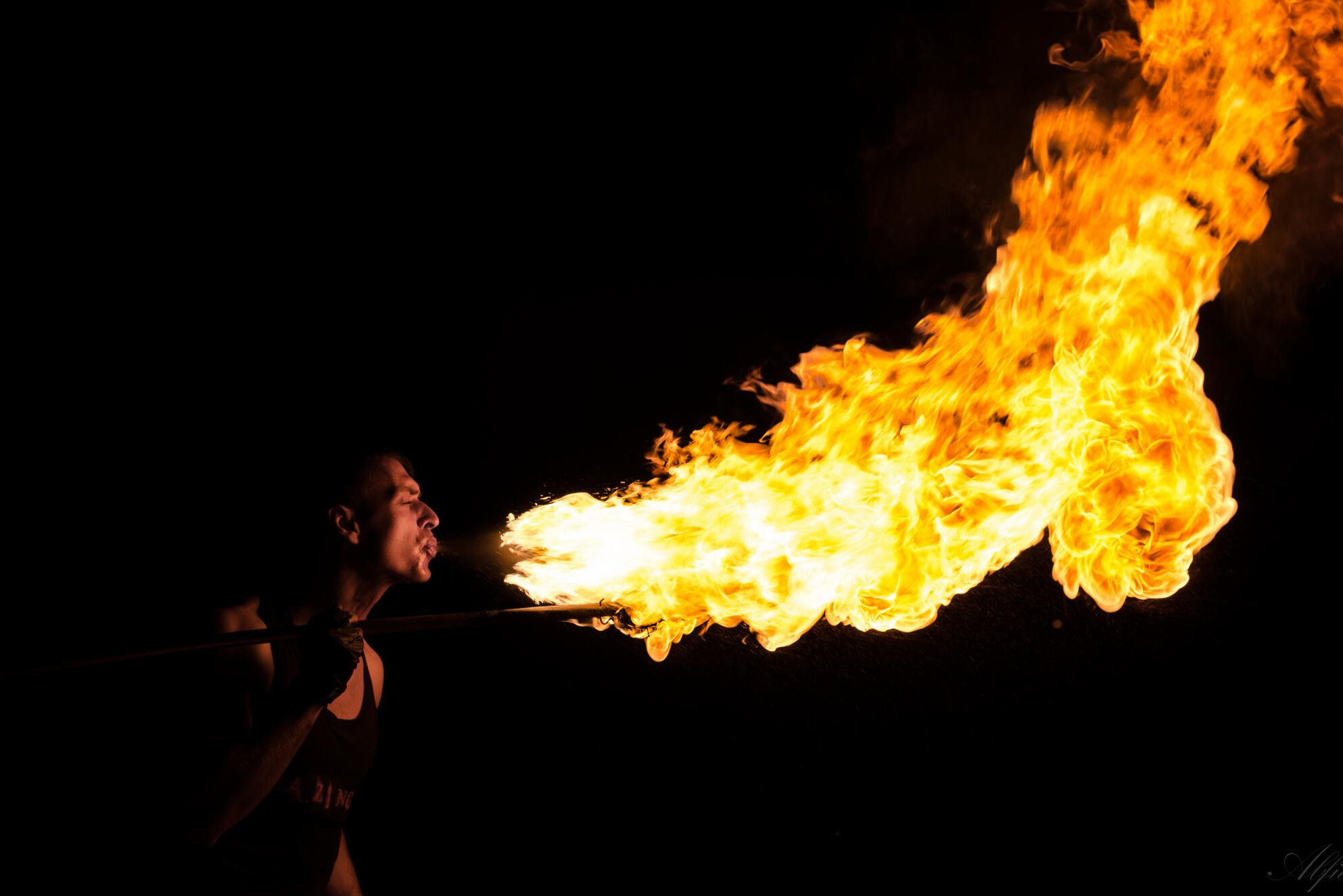 A fire breather blows flames in the dark.