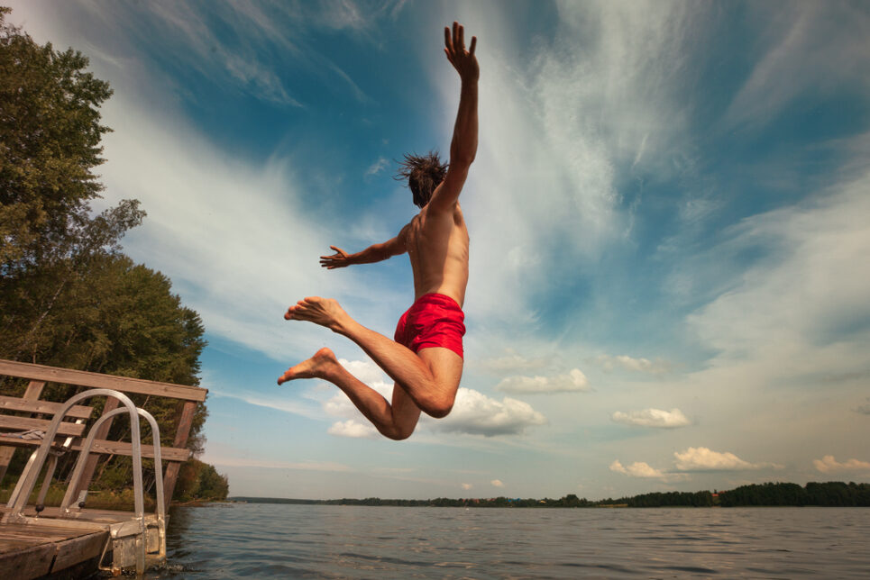 A young person jumps into the water from the end of a pier with arms spread wide.