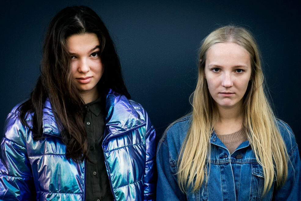 Two young girls stare straight ahead with serious expressions.