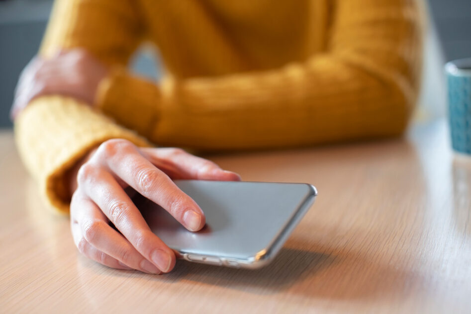 Someone sits at a table, about to set a mobile phone down.