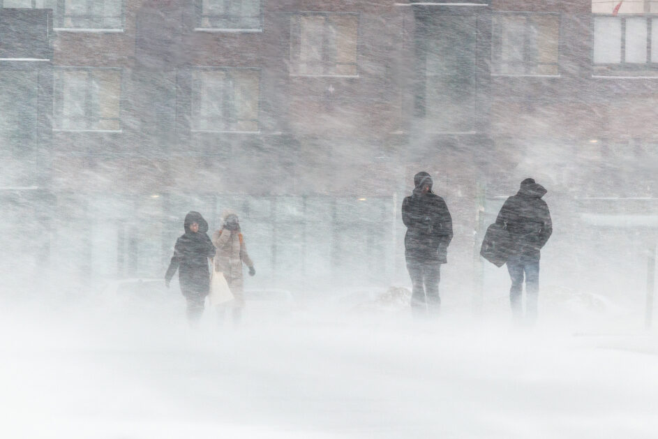 Four people walk down a street in heavy snowfall.
