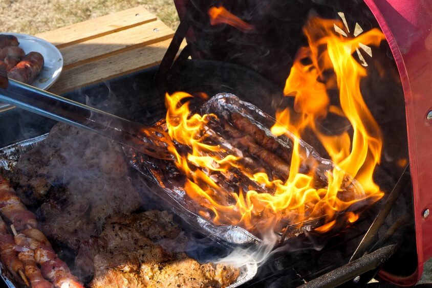 Sausages on a foil tray burning in a charcoal grill.