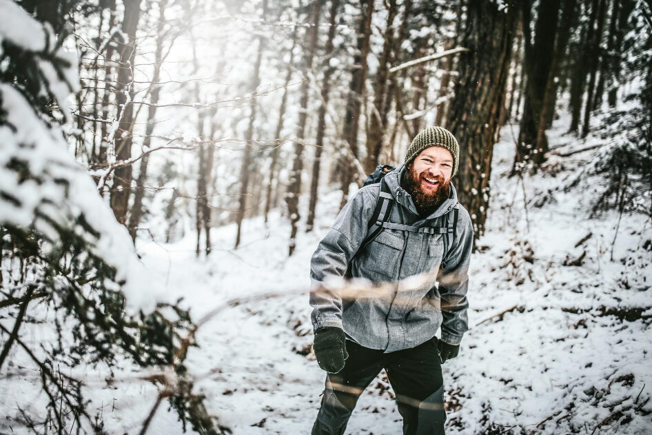 A smiling man walks along a snowy forest path.