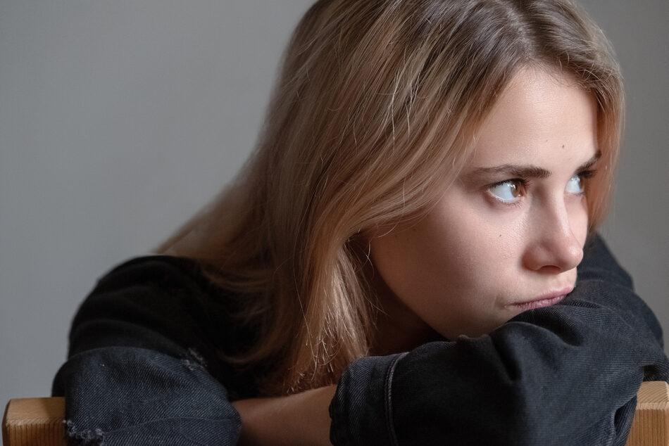 A young woman leans on her arm, looking thoughtfully to the side.