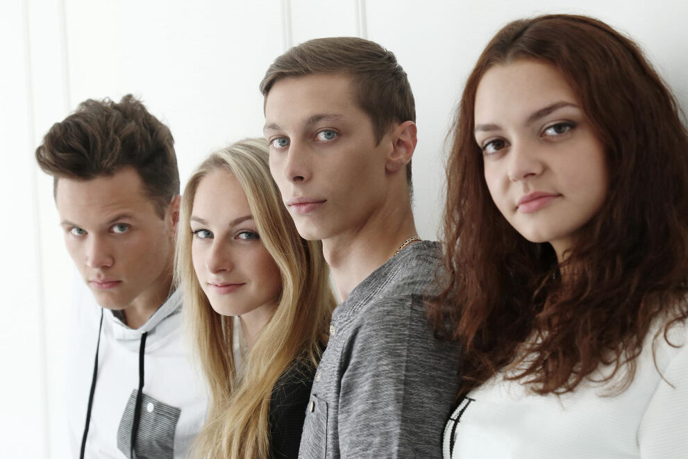 Two young women and two young men stand against a wall, looking straight ahead with determined expressions.