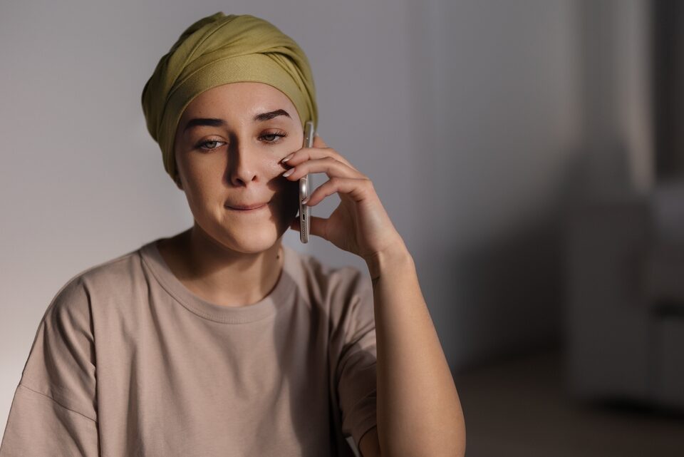 A young woman wearing a headscarf holds a phone to her ear, looking thoughtful.