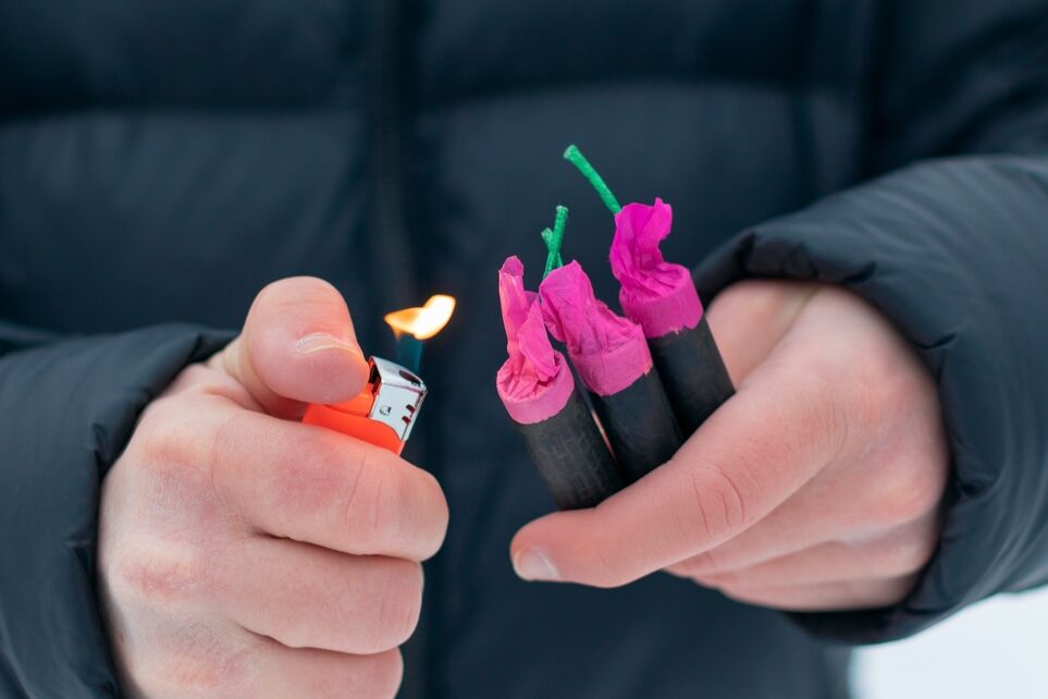 Firecrackers in one hand and a lighter with a flame in the other.