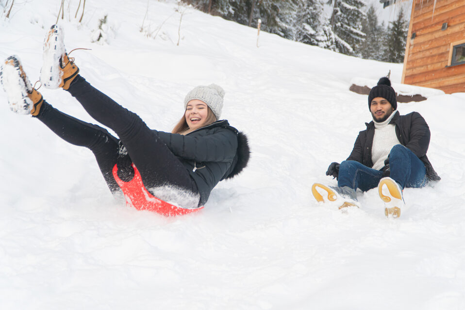 A smiling young woman and man slide down a snowy slope on a sled.