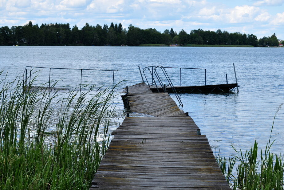 A young man wearing a life jacket helps a young woman tighten hers. A jet ski is visible in the water in the background.