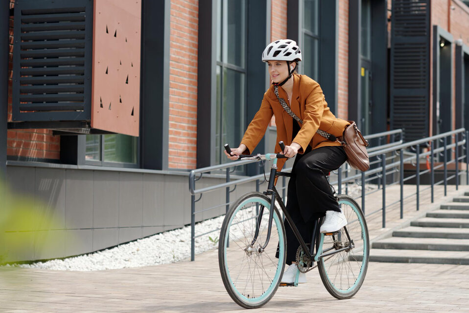 A woman wearing a bicycle helmet rides past a building that looks like a school.