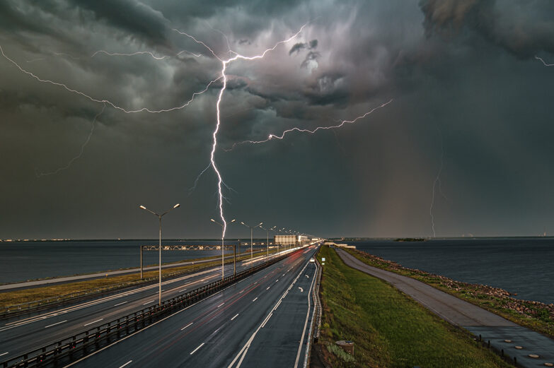 A thunderstorm at night. A vertical lightning bolt strikes the ground from dark clouds above a coastal road.