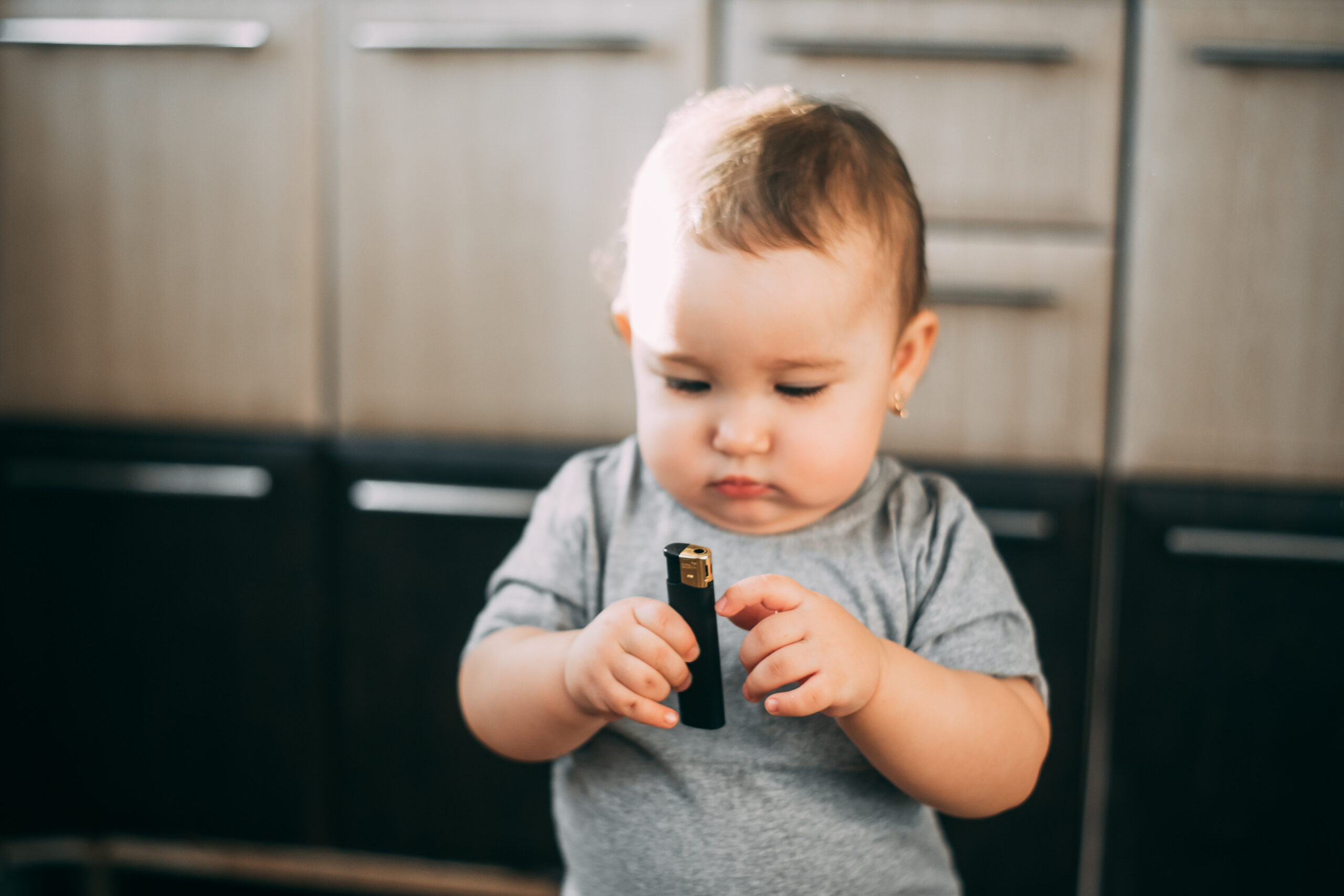 A toddler holding a small lighter and examining it closely.
