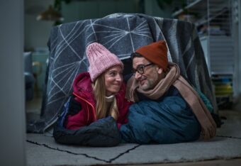 Nainen ja mies vilteistä pöydän päälle tehdyn teltan alla sisällä talvivaatteet päällä.