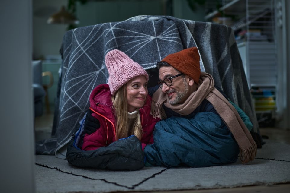 Nainen ja mies vilteistä pöydän päälle tehdyn teltan alla sisällä talvivaatteet päällä.