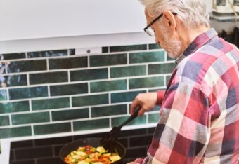 Ikääntynyt mies laittaa liedellä ruokaa ja lieden yläpuolella on kiinni liesivahti.