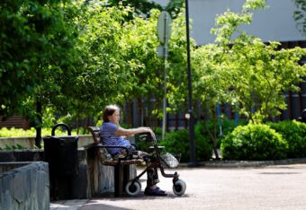 Vanhempi nainen istuu puiston penkillä rollaattorin kanssa.